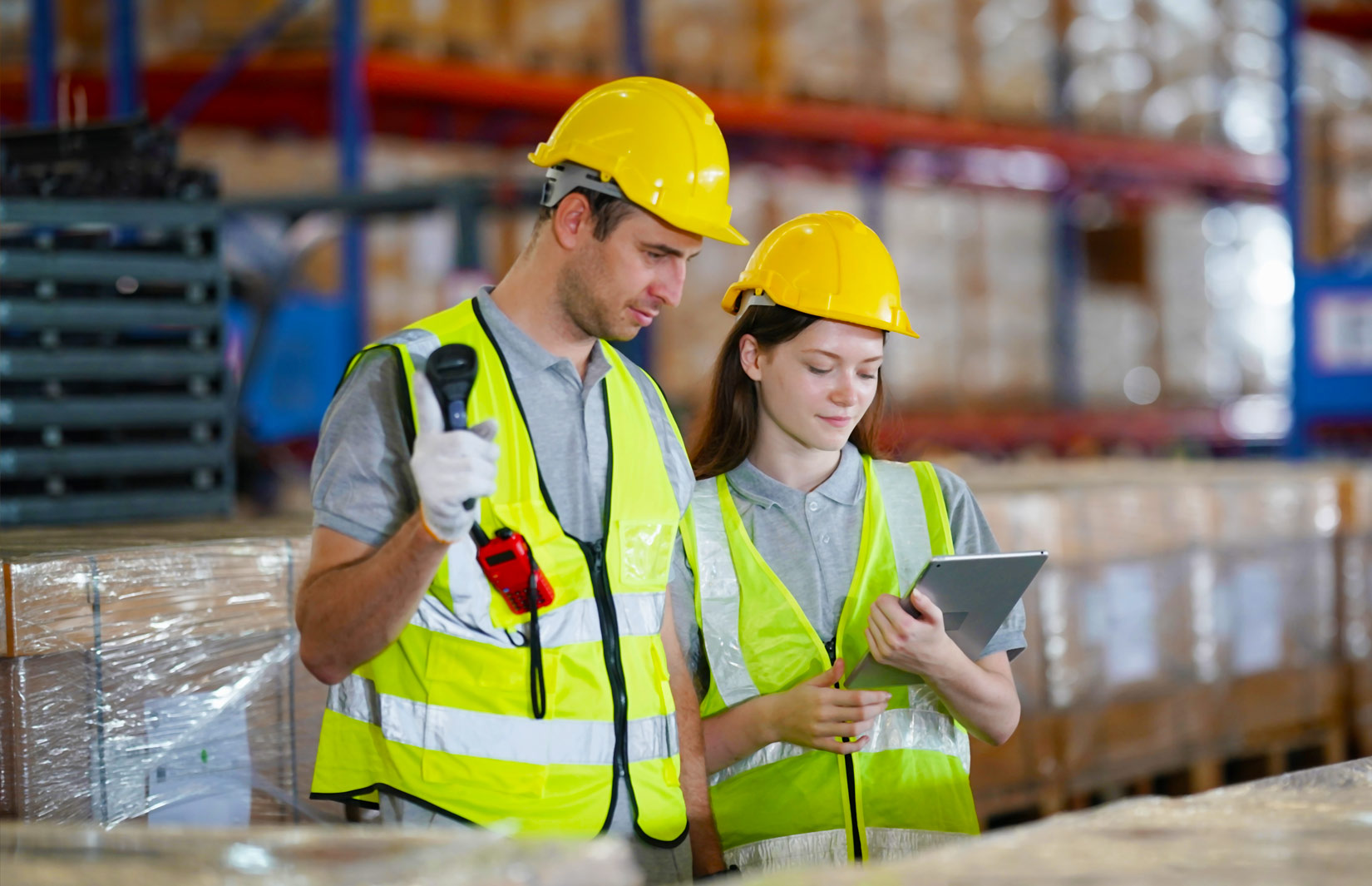 Zwei Mitarbeitende stehen vor einer Palette mit Kartons und schauen auf ein Notepad