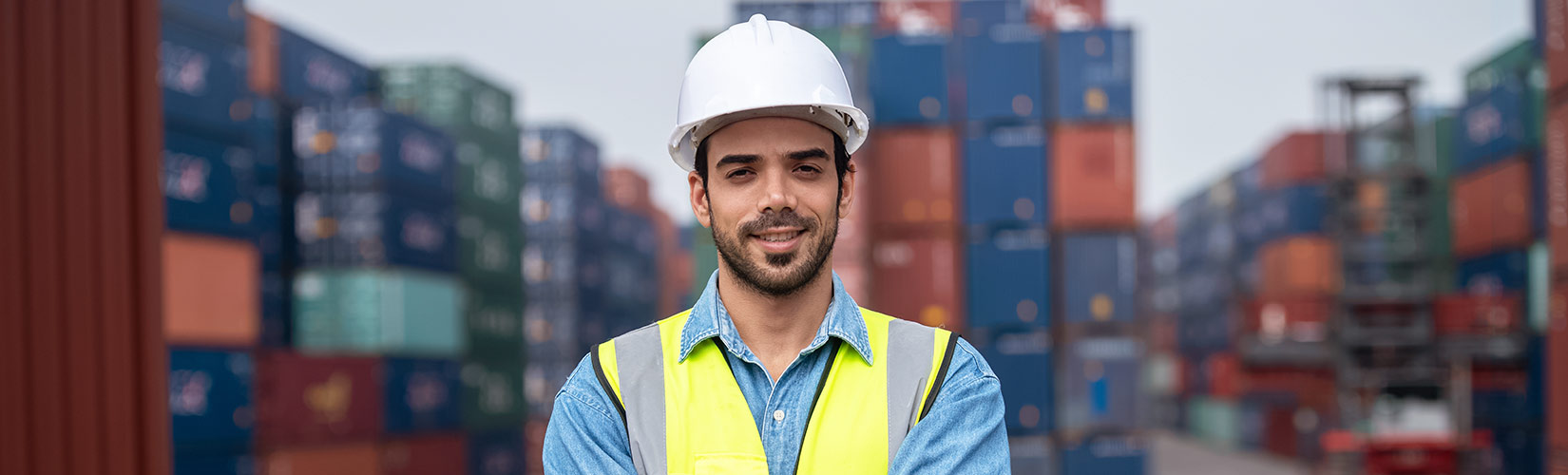 Mitarbeiter mit Warnweste und Helm vor einem Container-Terminal