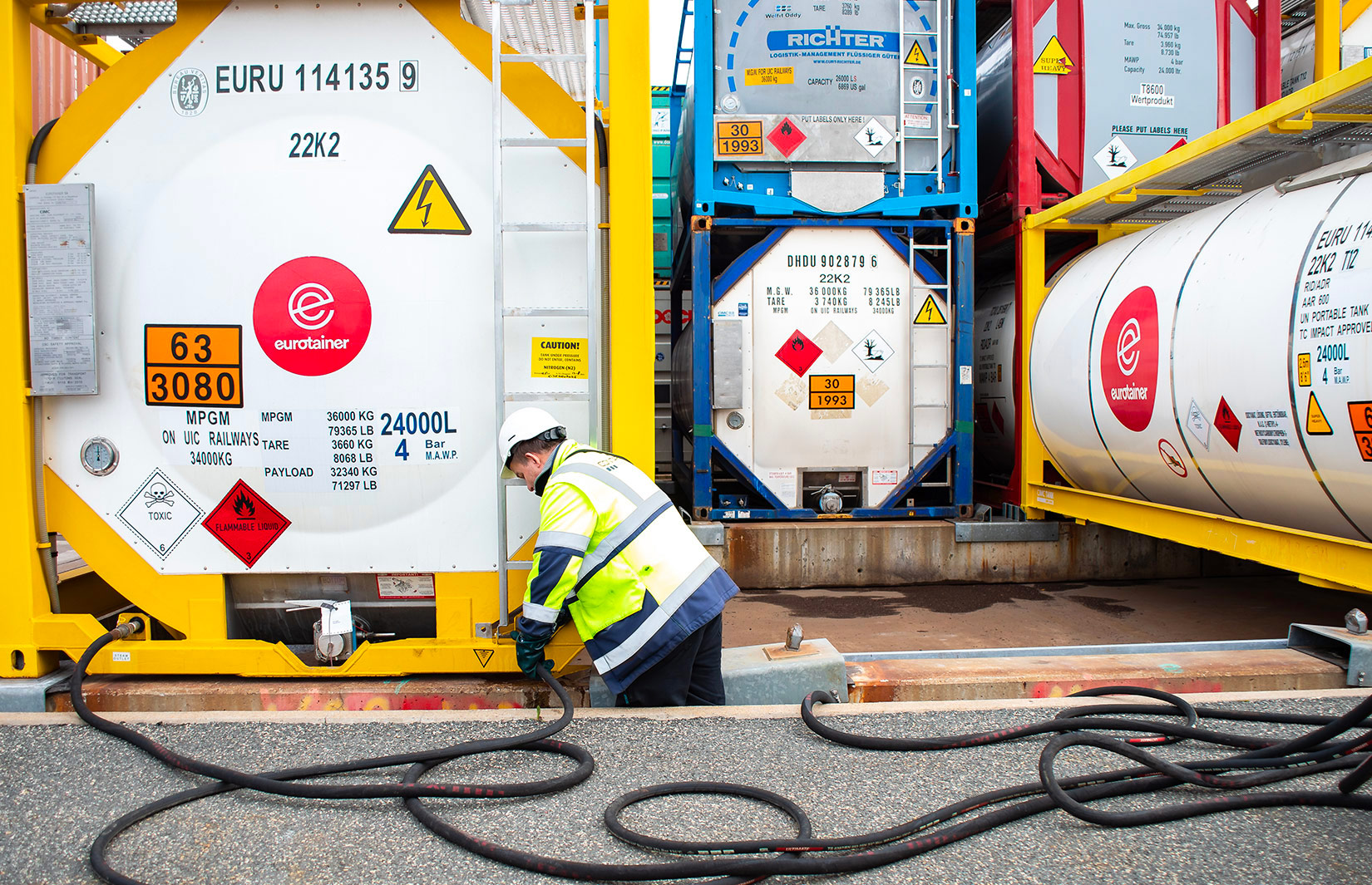 Mitarbeiter mit Helm und Warnweste arbeitet an Tankcontainern