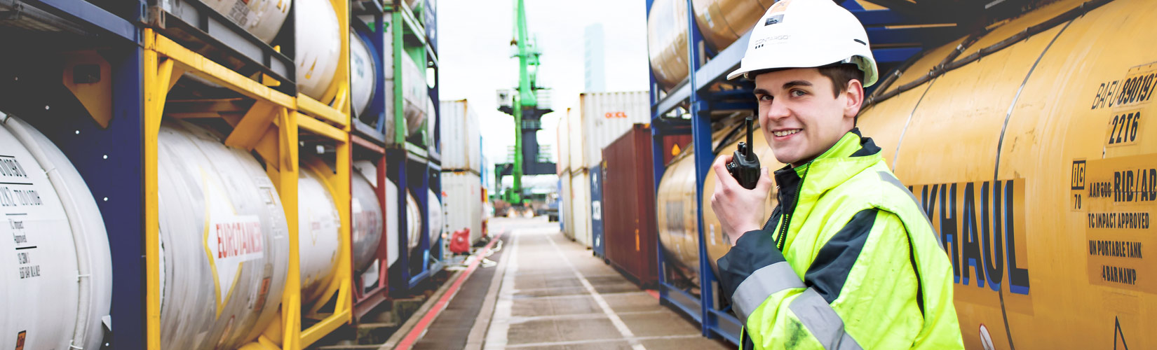 Mitarbeiter steht mit einem Funkgerät zwischen Containerstapel