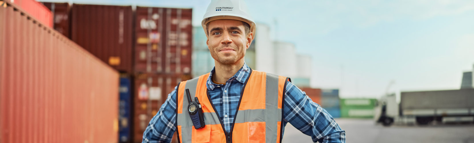 Mitarbeiter in Warnweste und Helm vor Container-Terminal