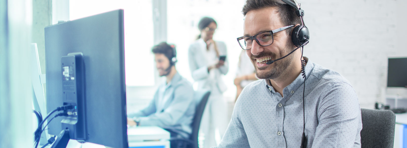 Smiling employee with headset in front of a monitor