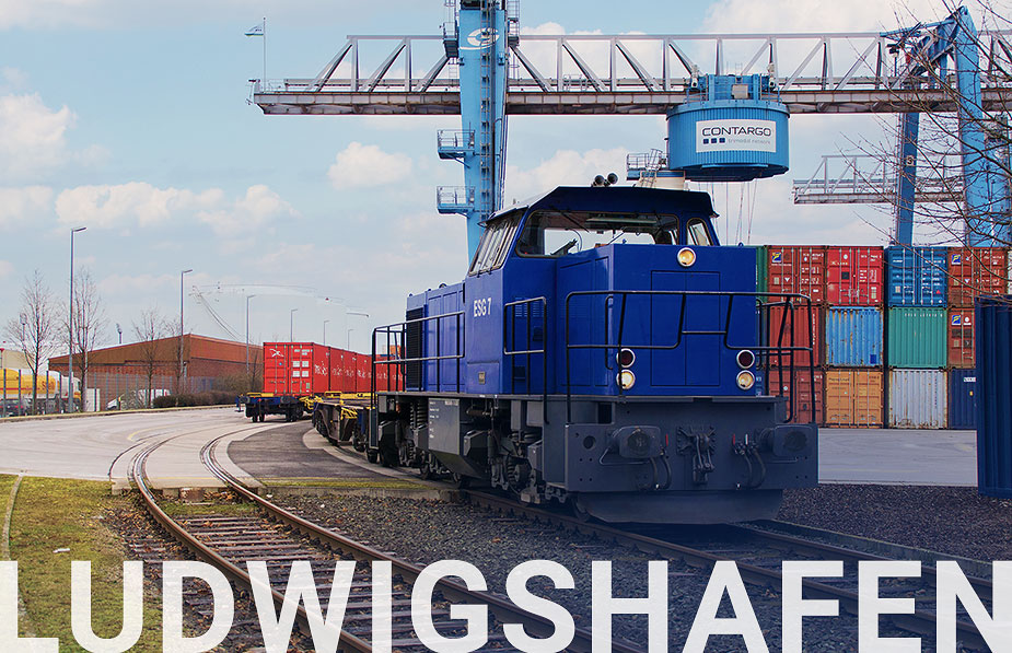 Blaue Lok eines Güterzugs. Im Hintergrund ein Container Terminal und ein Kran.