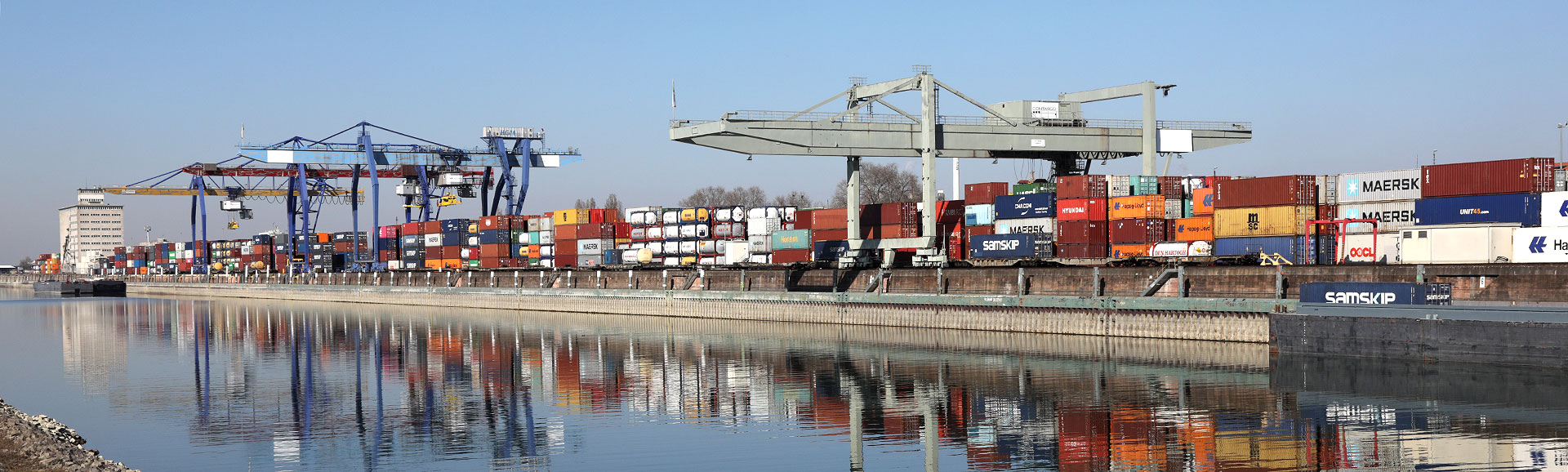 Fluss im Vordergrund mit Container-Terminal und Krananlagen im Hintergrund