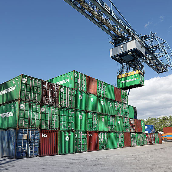 Gestapelte Container in grün und braun. Darüber ein Kran.