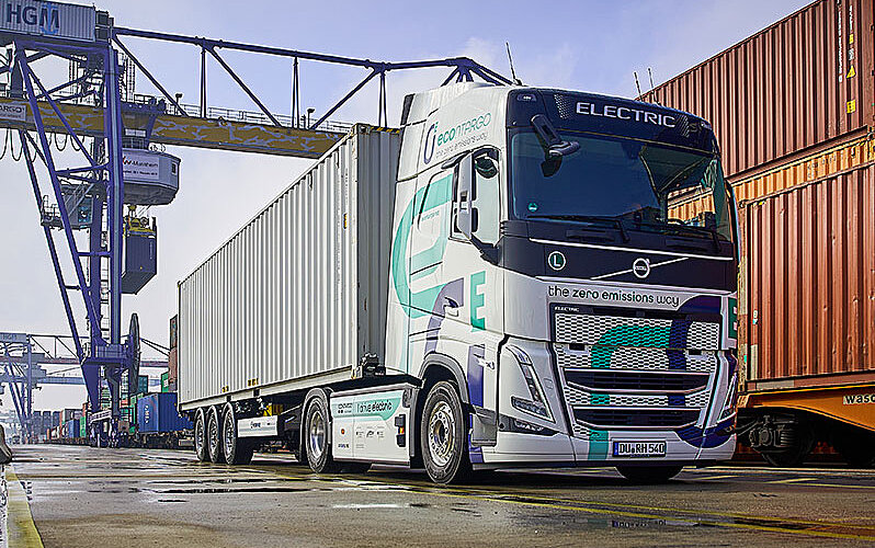 econtargo E-Lkw auf dem Container-Terminal mit Krananlage im Hintergrund