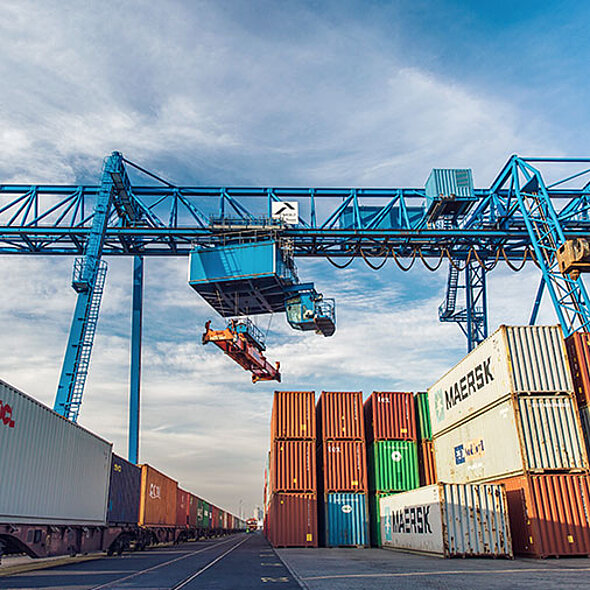 Containerstapel und Container-Zug mit Krananlage im Hintergrund