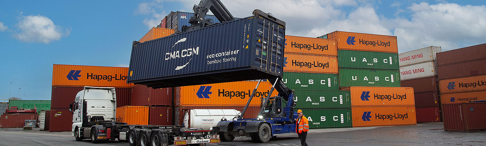 Reachstacker belädt einen Lkw mit einem blauen Container auf einem Container-Terminal