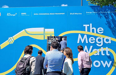 Menschen im Freien bei blauem Himmel vor blauer Wand mit dem Spruch "The Mega Watt Show"