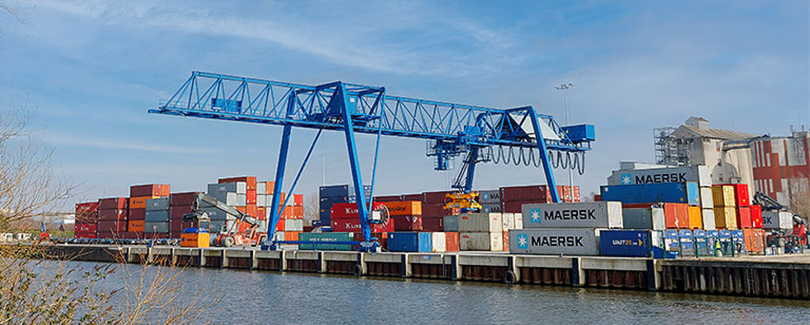 Fluss im Vordergrund mit einem Kran und Containerstapel im Hintergrund