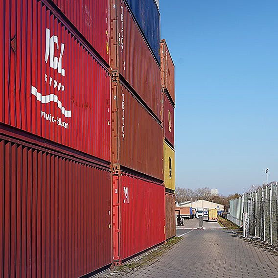 Wand mit gestapelten roten und brauen Containern. Geschäftsgebäude klein im Hintergrund.