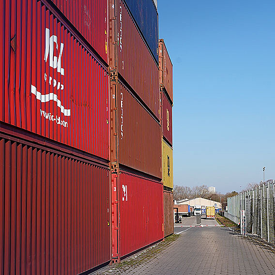 Wand mit gestapelten roten und brauen Containern. Geschäftsgebäude klein im Hintergrund