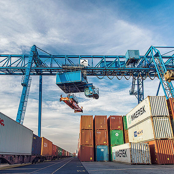 Container Terminal mit blauem Kran. Gestapelte Container und Containerzug darunter.