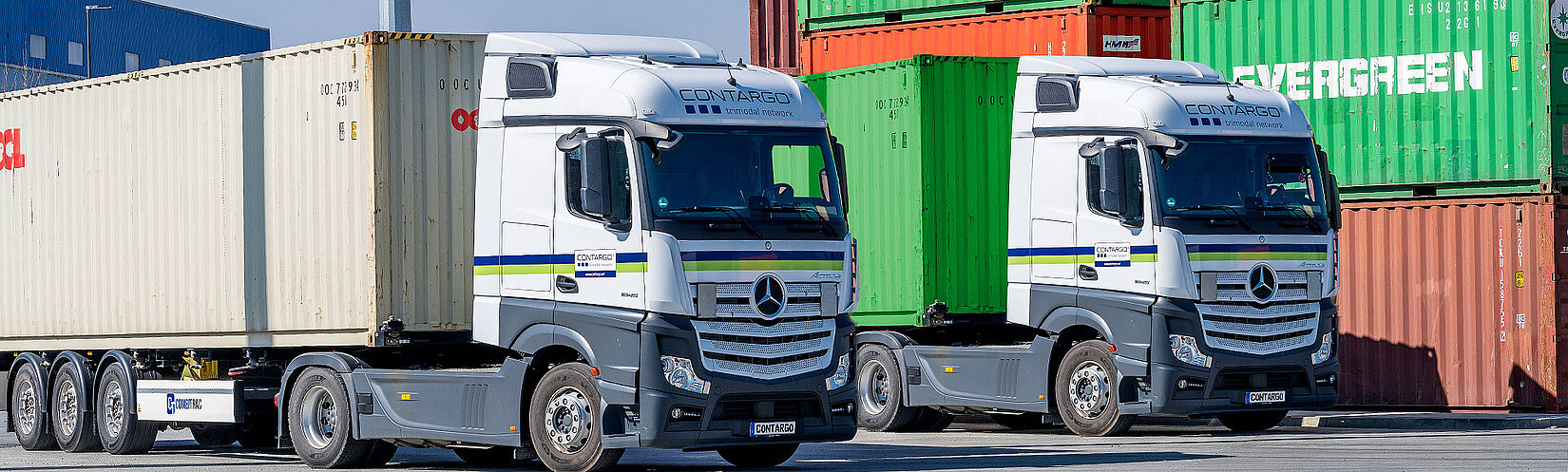 Zwei beladene Contargo Lkw vor gestapelten Containern