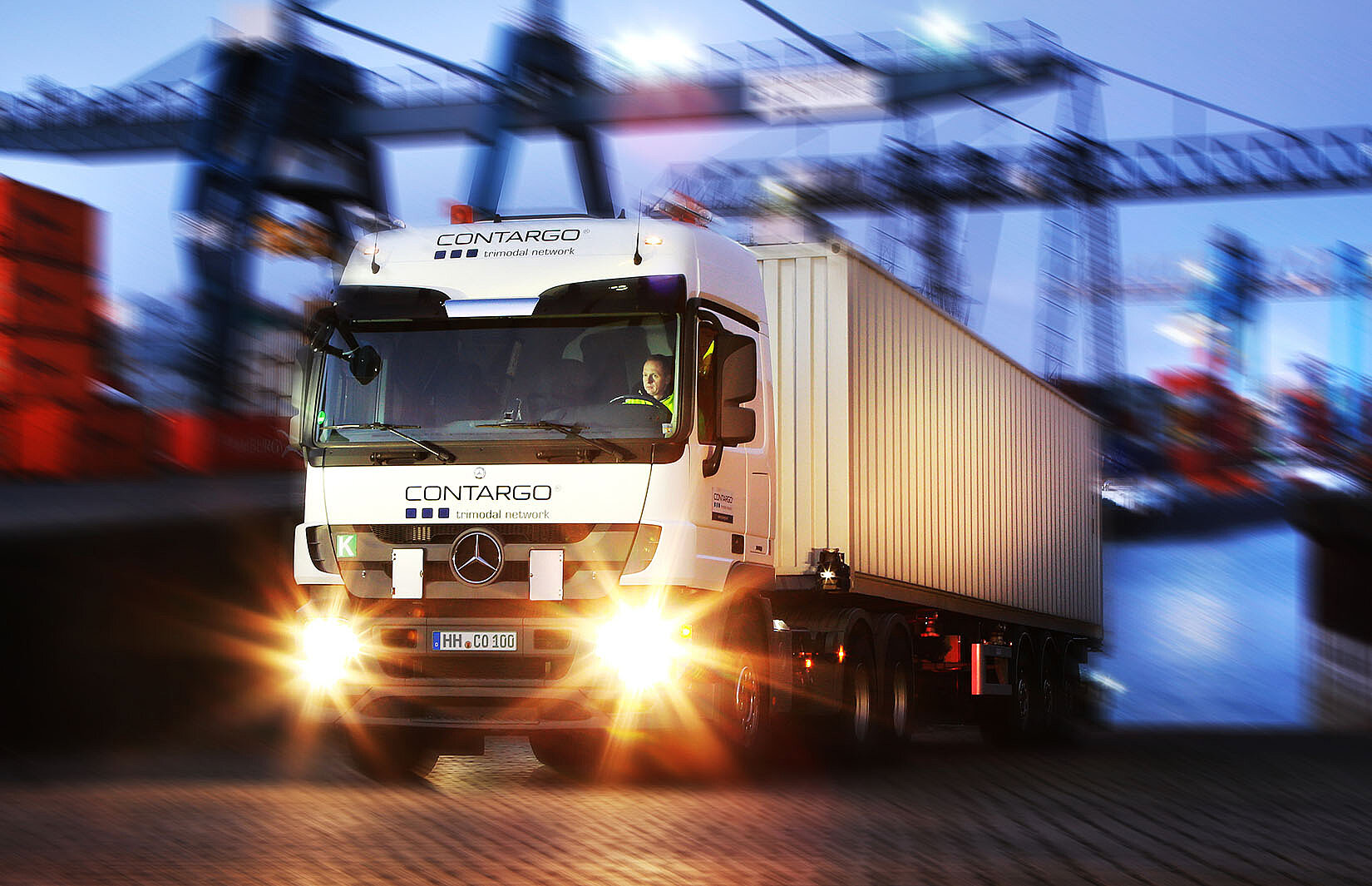 Lkw mit Container mit Kränen im Hintergrund