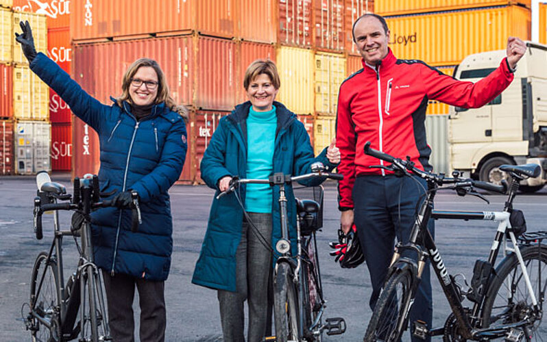 Jürgen Albersmann und zwei Mitarbeiterinnen mit Fahrrädern vor Containerstapel