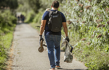 Mitarbeiter von hinten mit Greifzange und gefüllten Müllbeutel in der Hand