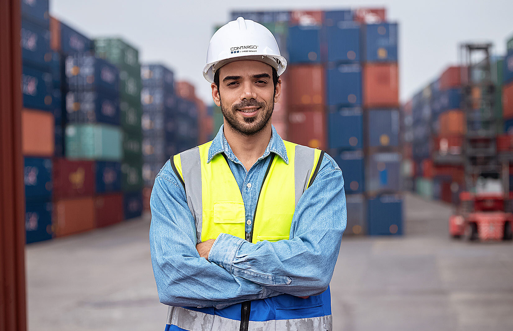 Berufseinsteiger mit Warnweste und Helm vor einem Container-Terminal