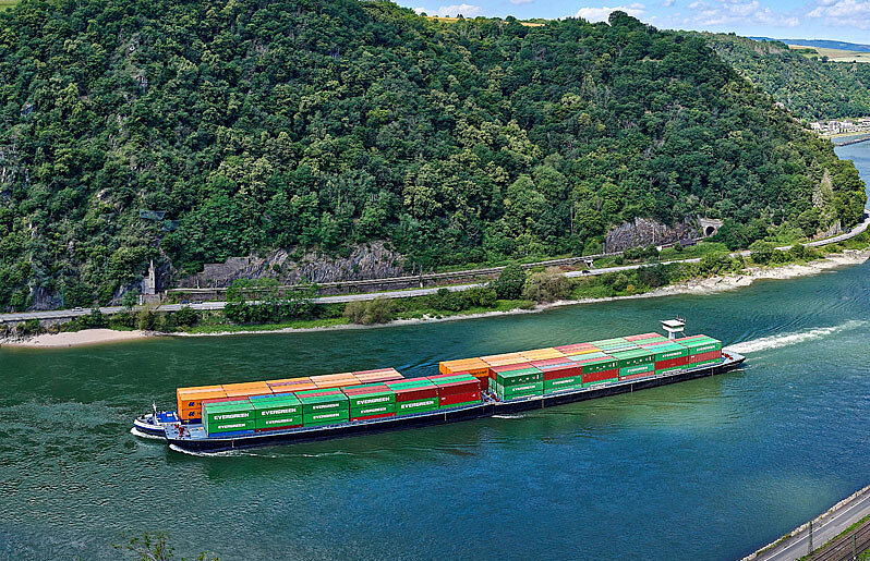 Binnenschiff auf einem Fluss mit Waldlandschaft im Hintergrund