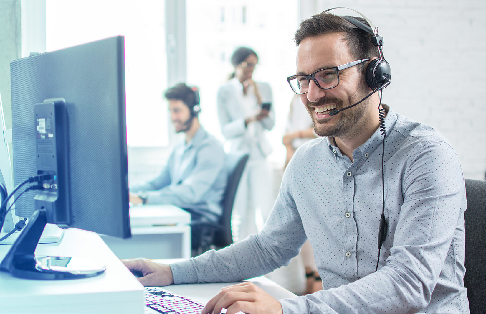 Büro-Mitarbeiter mit Headset sitzt am PC