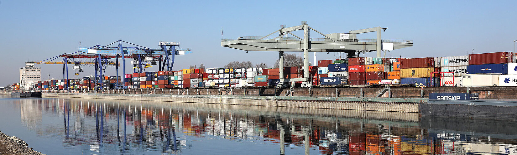 Fluss im Vordergrund mit Container-Terminal und Krananlagen im Hintergrund