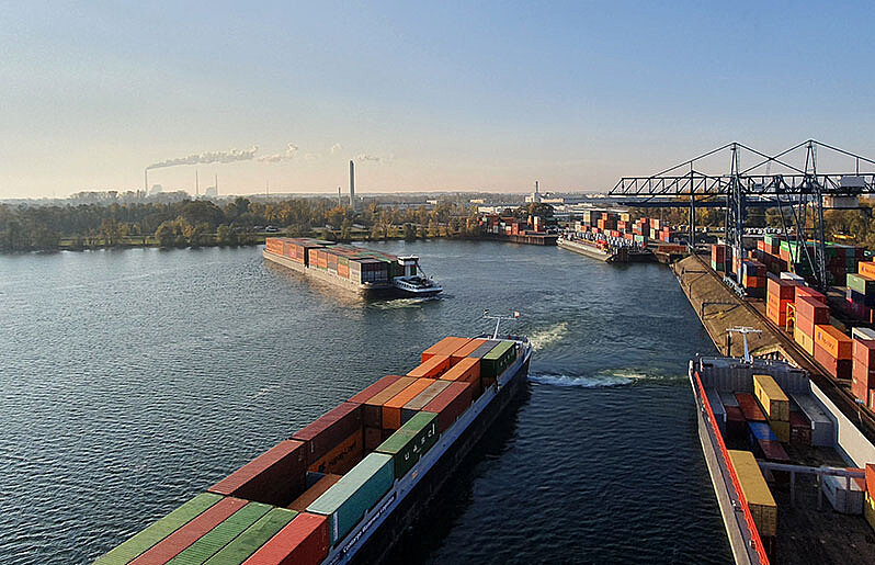 Zwei Binnenschiffe auf dem Fluss und zwei Binnenschiffe, die an einem Container Terminal anlegen